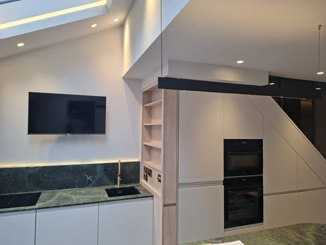 Kitchen with recessed downlights, a linear pendant and concealed lighting around the rooflight and splashback.