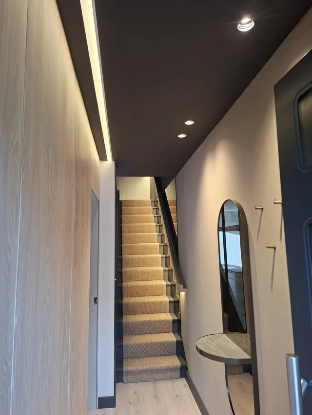 Hallway and staircase with recessed downlights and concealed linear lighting.